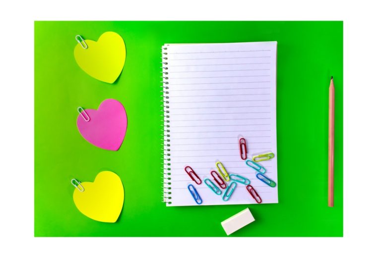 Un carnet vide entouré de cœurs colorés et de trombones sur un fond vert.