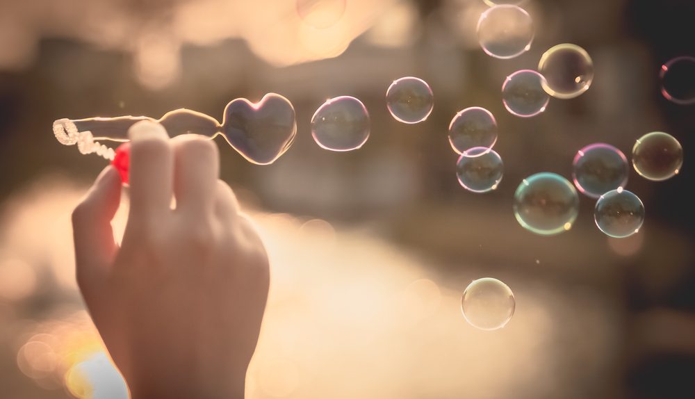 Une main souffle des bulles en forme de cœur au coucher du soleil.