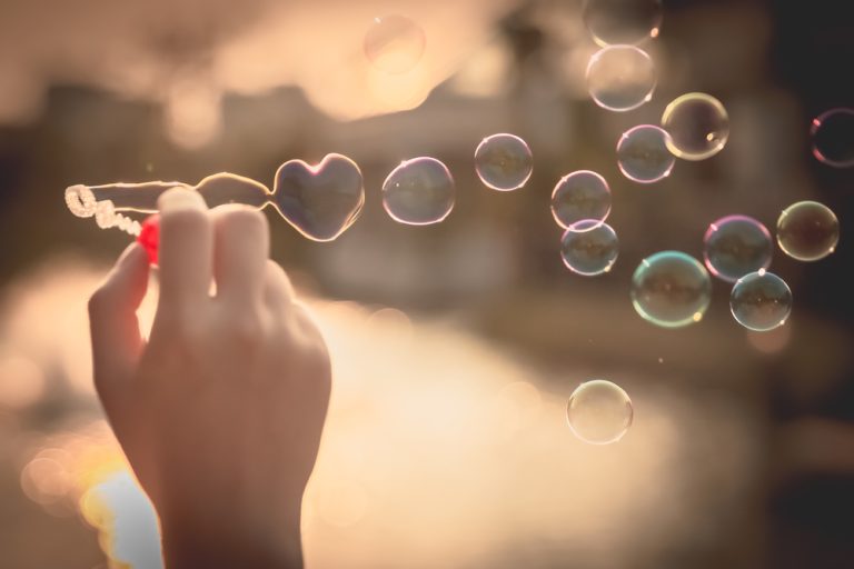 Une main souffle des bulles en forme de cœur au coucher du soleil.