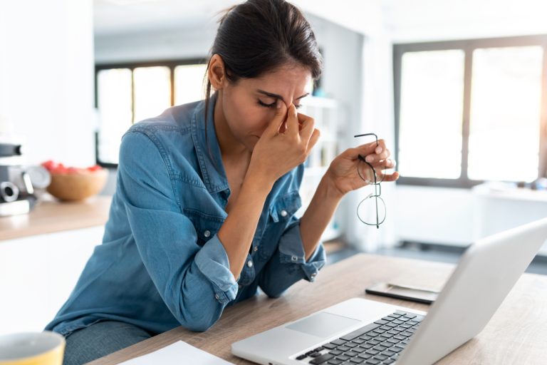 Une femme fatiguée se tient le visage devant son ordinateur portable.