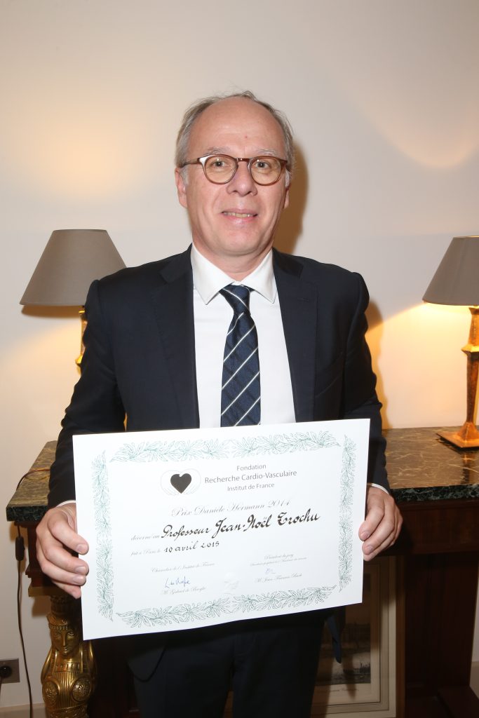 Homme en costume tenant un certificat lors d’une cérémonie officielle.