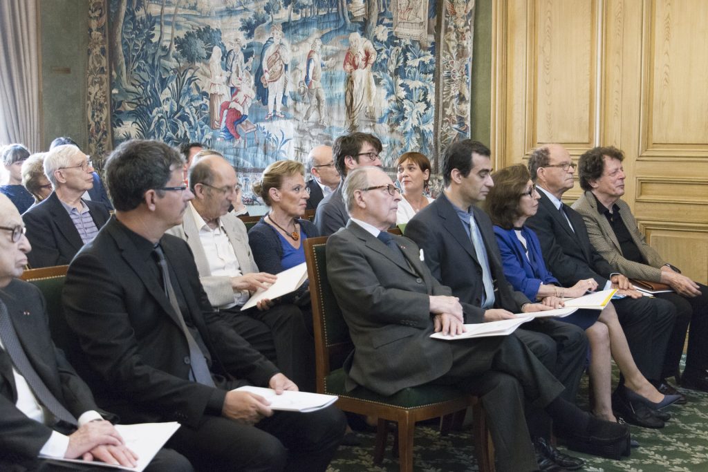 Des invités assistent à une cérémonie officielle dans une salle élégante.