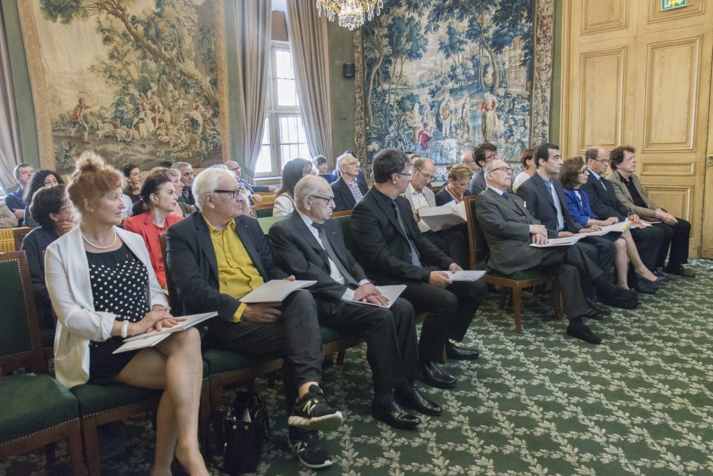Des invités assistent à une cérémonie officielle dans une salle élégante.