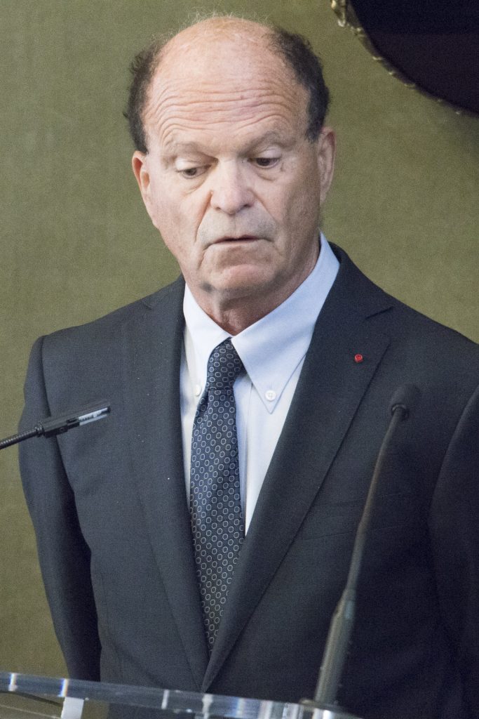 Un homme en costume prend la parole derrière un pupitre lors d’un événement officiel.