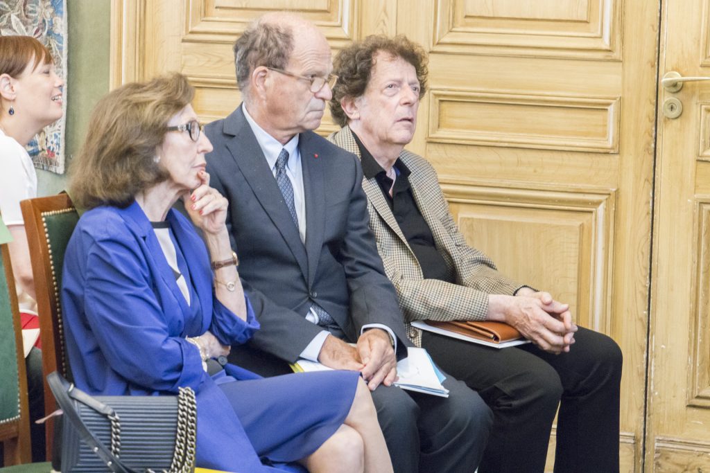 Trois personnes assises écoutent attentivement lors d’un événement officiel.