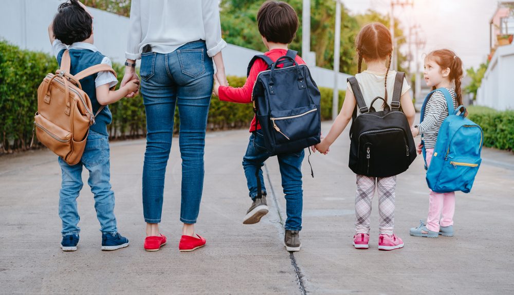 Adulte accompagnant plusieurs enfants avec des sacs à dos sur le chemin de l’école.
