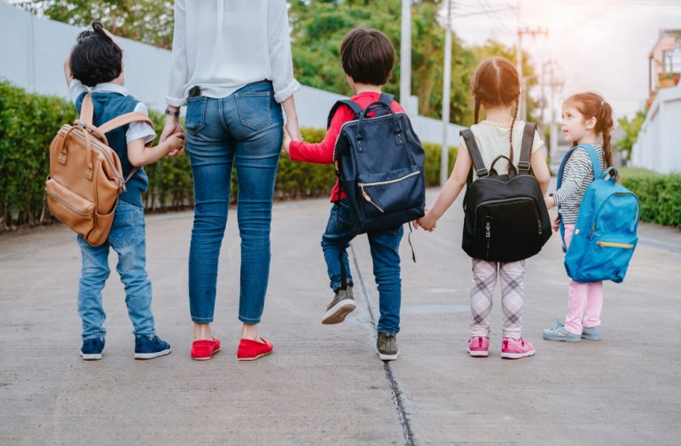 Adulte accompagnant plusieurs enfants avec des sacs à dos sur le chemin de l’école.