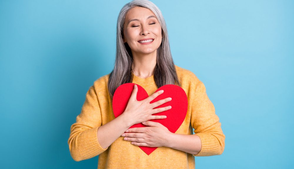 Femme souriante tenant un cœur rouge contre elle.