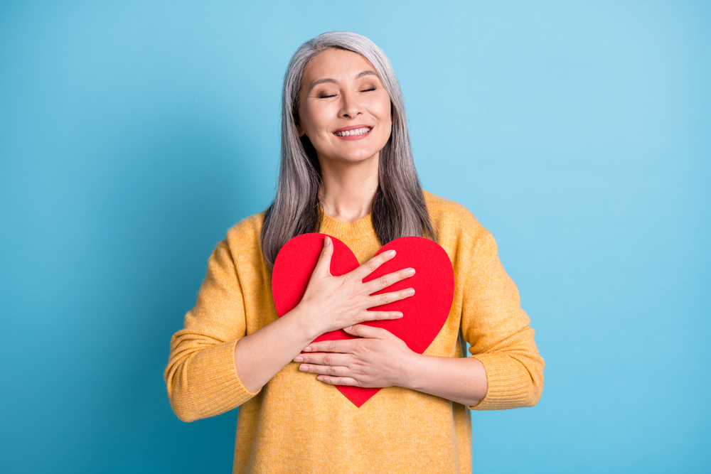 Femme souriante tenant un cœur rouge contre elle.