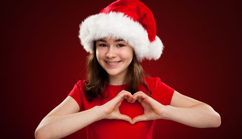 Jeune fille portant un bonnet de Noël formant un cœur avec ses mains.