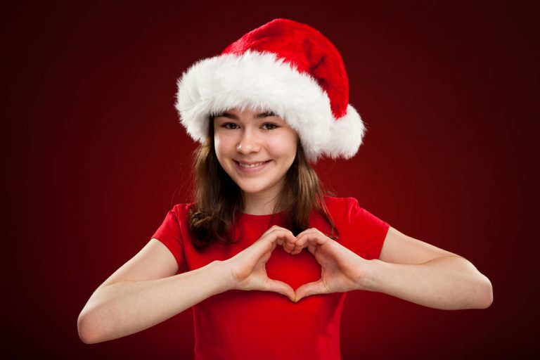 Jeune fille portant un bonnet de Noël formant un cœur avec ses mains.