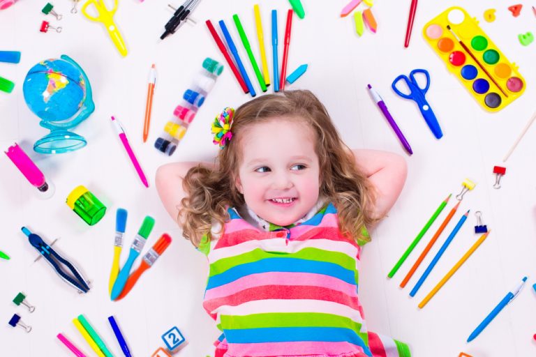 Petite fille allongée entourée de fournitures scolaires colorées.