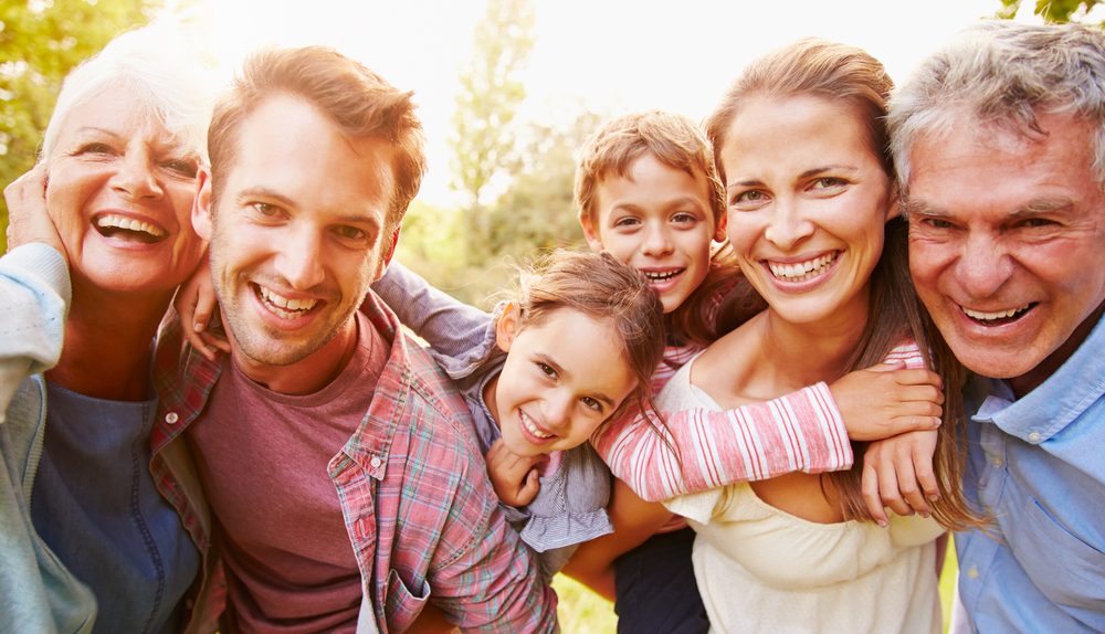 Famille multigénérationnelle souriante réunie en extérieur.