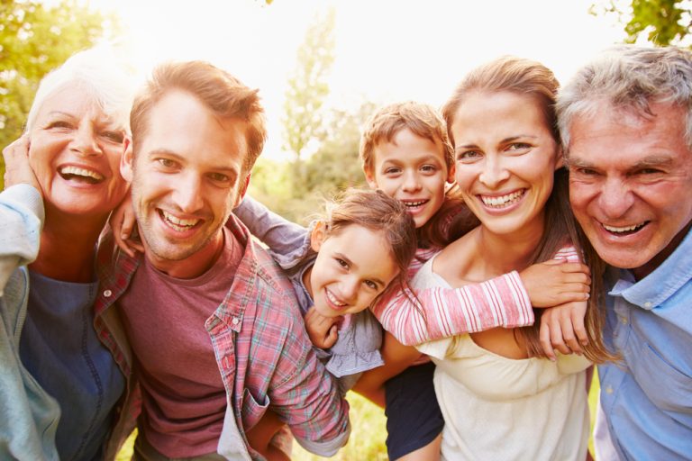 Famille multigénérationnelle souriante réunie en extérieur.