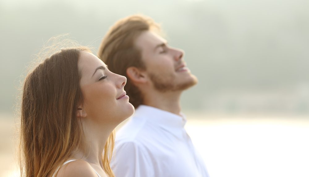 Jeune femme et jeune homme respirant profondément les yeux fermés dans un environnement apaisant.