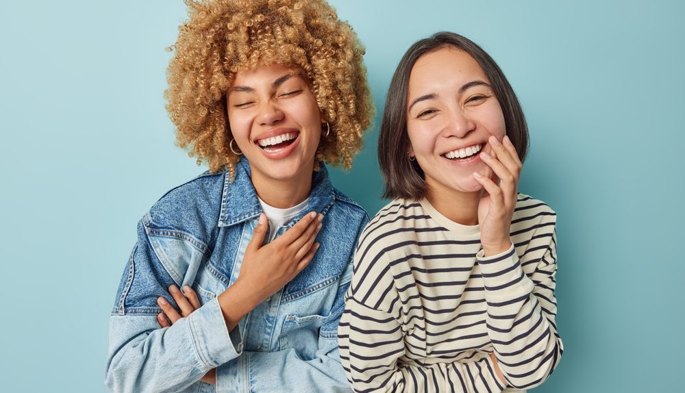 Deux jeunes femmes souriantes riant ensemble devant un fond bleu clair.