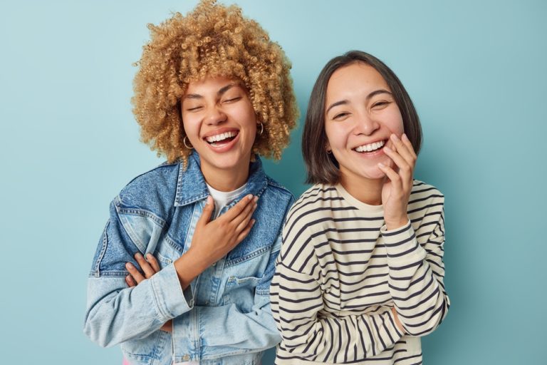 Deux jeunes femmes souriantes riant ensemble devant un fond bleu clair.
