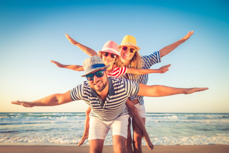 Famille souriante jouant sur la plage avec les bras écartés comme des avions.