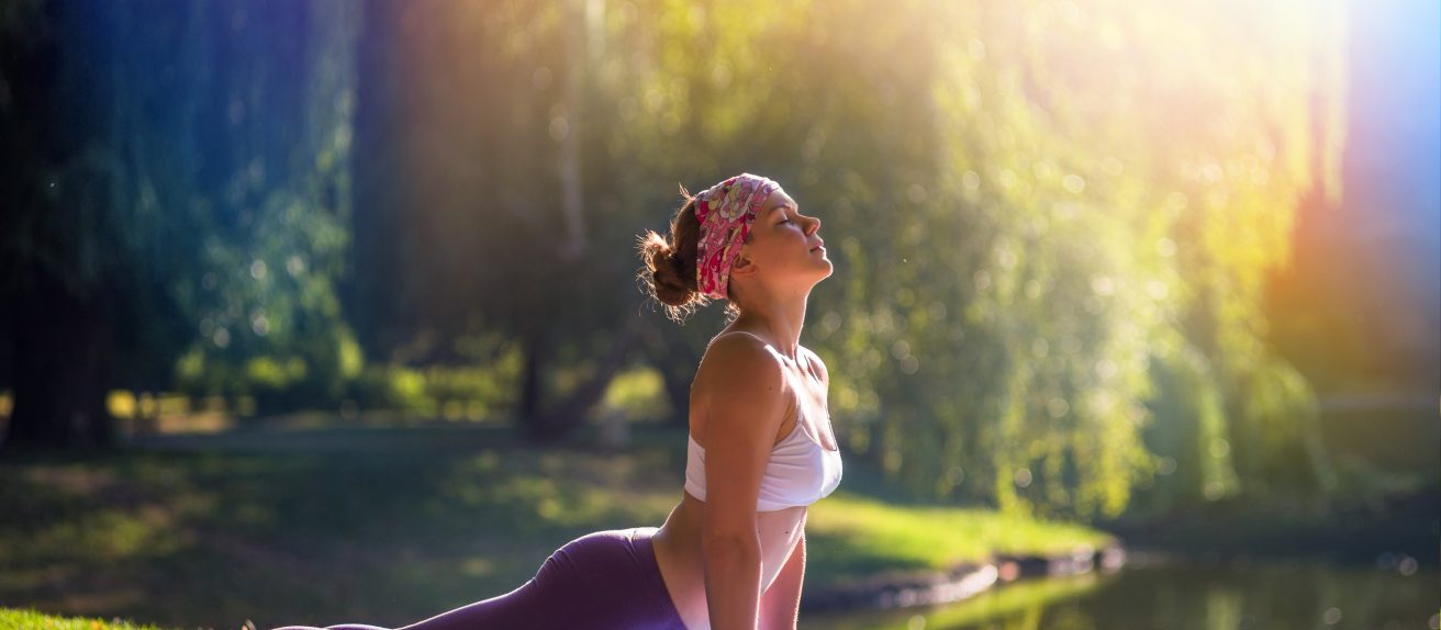 Femme pratiquant le yoga en plein air dans un parc pour favoriser le bien-être physique et mental.