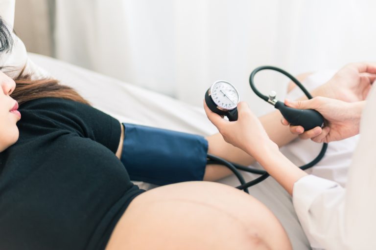 Femme enceinte lors d’un contrôle médical avec prise de tension artérielle pendant le suivi de grossesse.