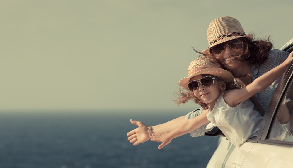 Mère et enfant souriants sortant d’une voiture près de la mer pour symboliser les vacances, le bien-être familial et la liberté.