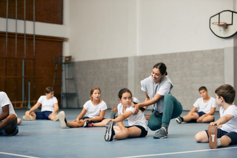 Professeure de sport aidant une élève pendant une séance d’étirements dans un gymnase scolaire.