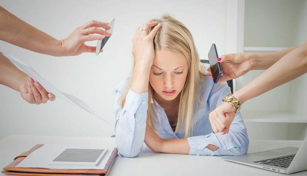 Femme stressée au bureau entourée de sollicitations professionnelles illustrant la surcharge mentale et le stress au travail.