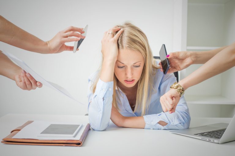 Femme stressée au bureau entourée de sollicitations professionnelles illustrant la surcharge mentale et le stress au travail.