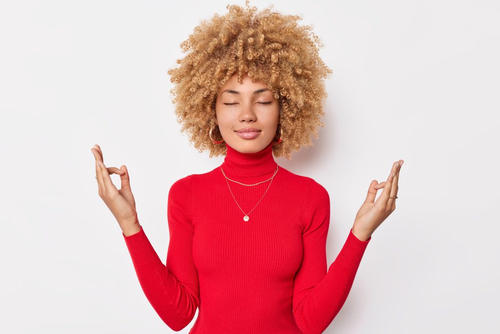 Jeune femme méditant les yeux fermés avec les mains en position de relaxation pour symboliser le bien-être mental et la sérénité.