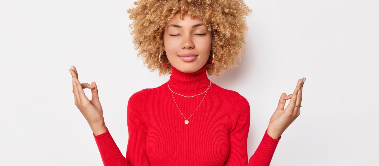Jeune femme méditant les yeux fermés avec les mains en position de relaxation pour symboliser le bien-être mental et la sérénité.