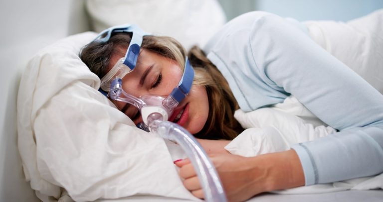 Femme dormant avec un masque de ventilation pour le traitement de l’apnée du sommeil.