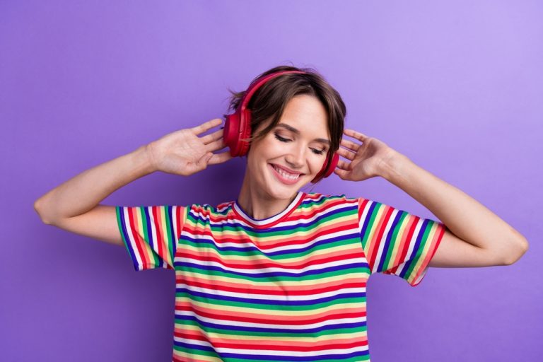 Jeune femme souriante écoutant de la musique avec un casque audio sur un fond violet.