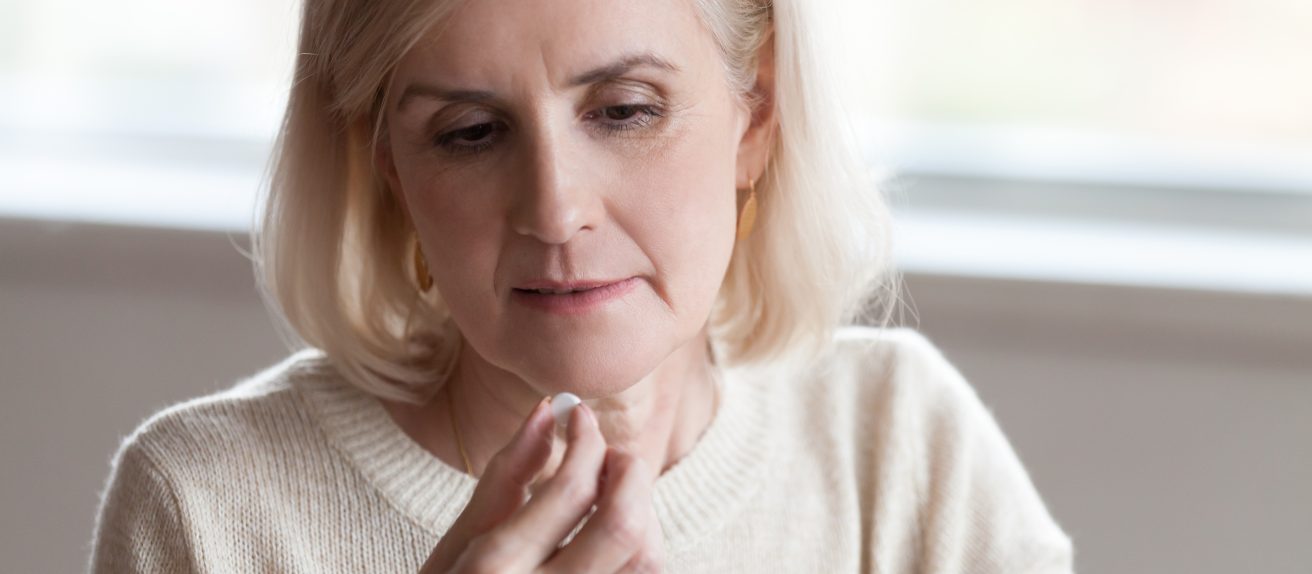 Femme mature tenant un comprimé et un verre d’eau pour illustrer la prise de traitement médical et le suivi de la santé.