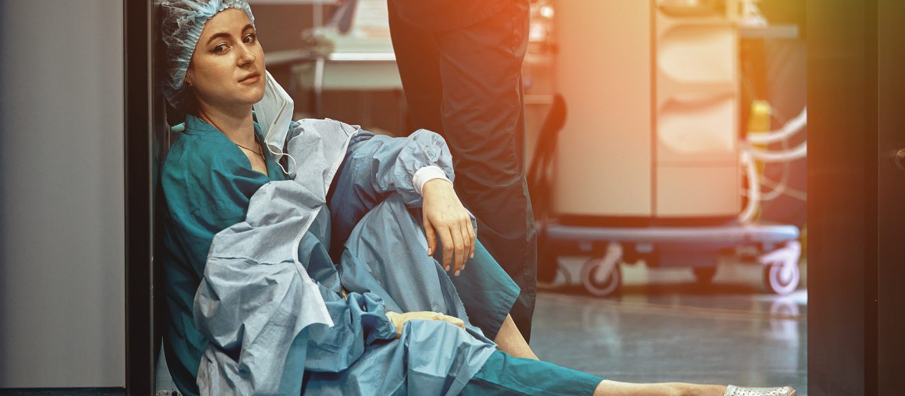 Soignante assise au sol dans un hôpital en état d’épuisement professionnel illustrant le burnout et ses conséquences sur la santé cardiovasculaire
