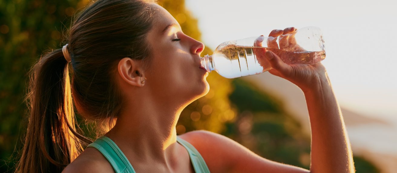 Femme buvant un verre d’eau par temps chaud illustrant l’importance de l’hydratation pour la santé cardiovasculaire
