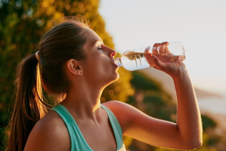 Femme buvant un verre d’eau par temps chaud illustrant l’importance de l’hydratation pour la santé cardiovasculaire