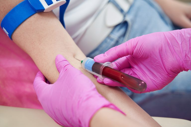 Prise de sang réalisée par un professionnel de santé portant des gants roses.