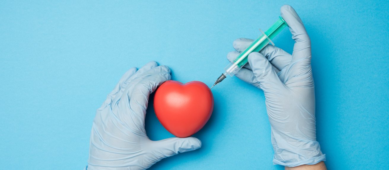Médecin tenant une seringue près d’un modèle de cœur illustrant une coronarographie