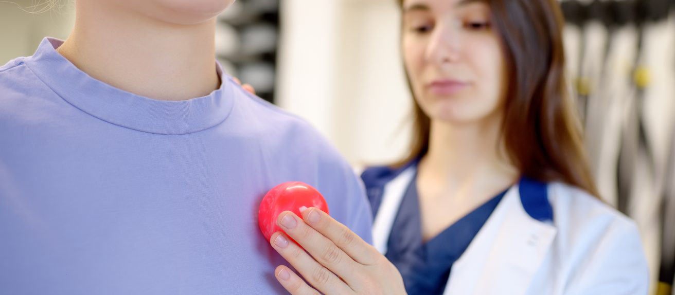 Médecin posant la main près du cœur d’un patient avec un modèle de cœur illustrant l’implantation d’un pacemaker