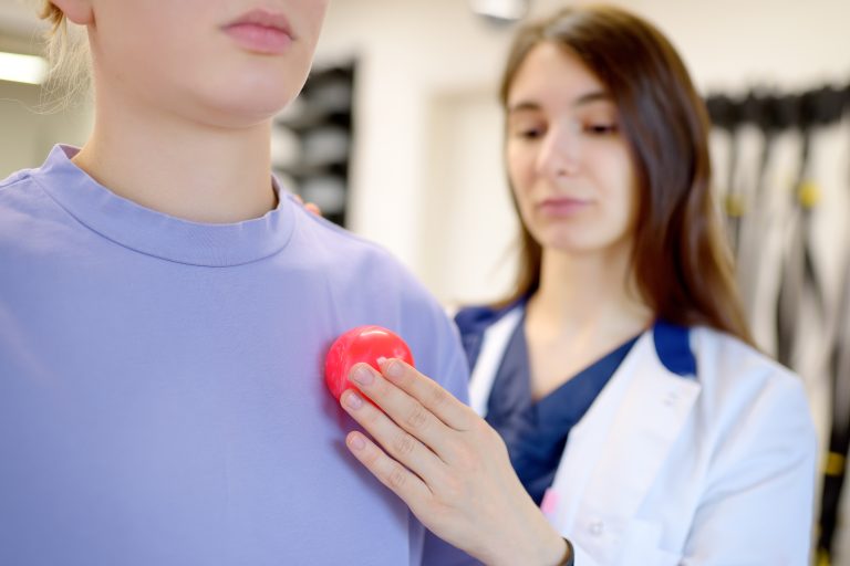 Médecin posant la main près du cœur d’un patient avec un modèle de cœur illustrant l’implantation d’un pacemaker