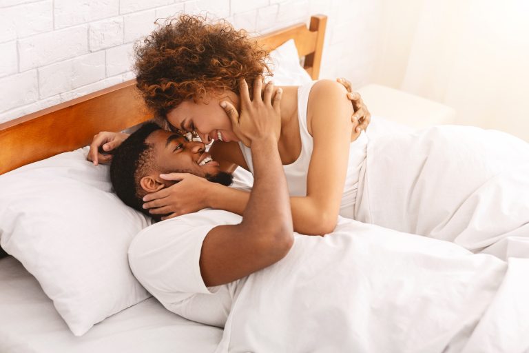 Couple souriant assis dans un lit illustrant le lien entre bien-être intime et santé cardiovasculaire