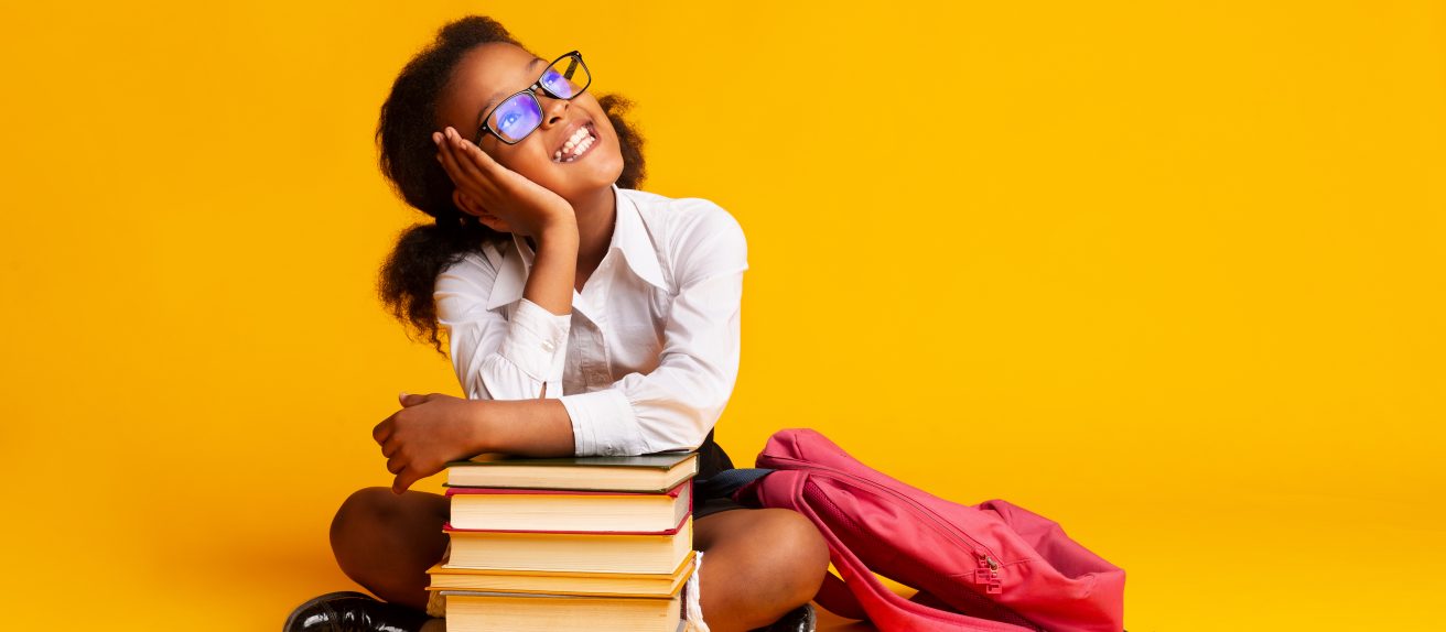 Petite fille souriante avec une pile de livres illustrant la santé des jeunes, l’éducation et l’importance de l’activité physique pour le cœur