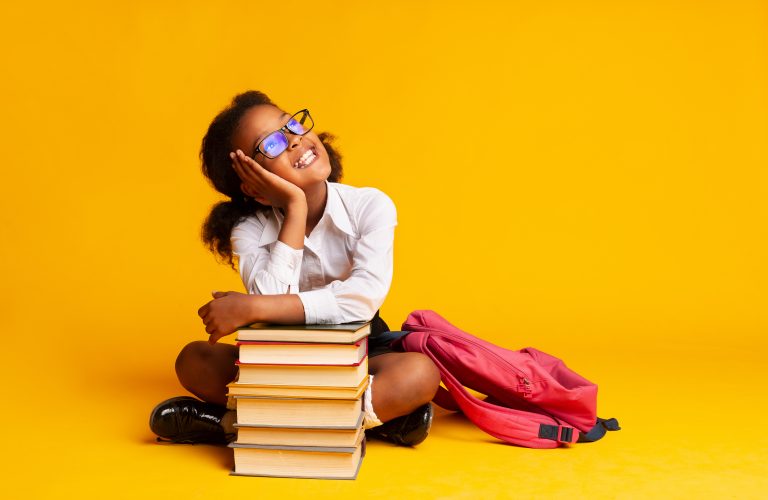 Petite fille souriante avec une pile de livres illustrant la santé des jeunes, l’éducation et l’importance de l’activité physique pour le cœur