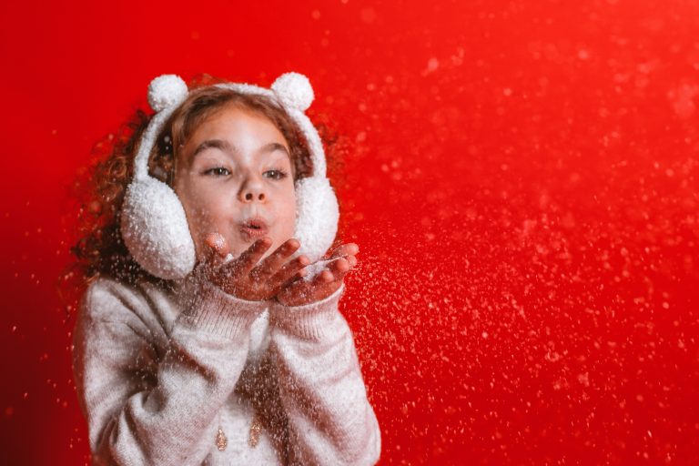 Petite fille soufflant des flocons de neige sur fond rouge de Noël pour symboliser la joie, l’espoir et la santé du cœur pendant les fêtes