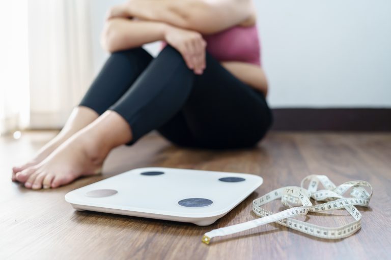 Femme déçue après s’être pesée illustrant les liens entre obésité, hypertension et risque de démence vasculaire
