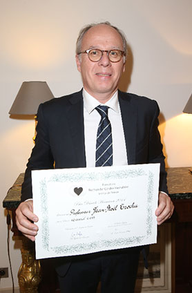 Homme en costume tenant un certificat lors d’une cérémonie officielle.