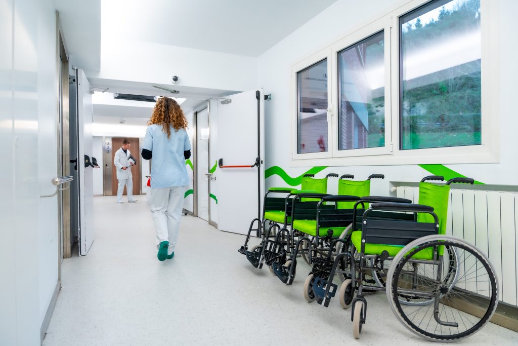 Couloir d’hôpital lumineux avec plusieurs fauteuils roulants alignés et du personnel soignant en arrière-plan.