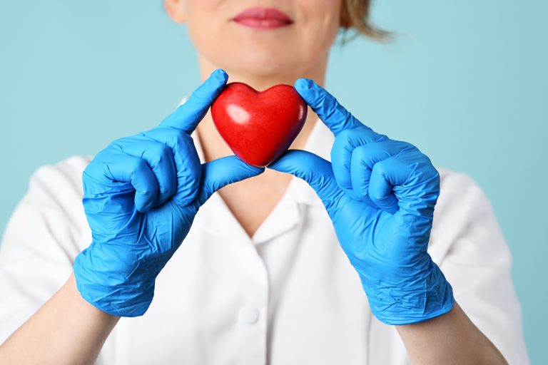 Professionnelle de santé tenant un cœur rouge avec des gants médicaux bleus.
