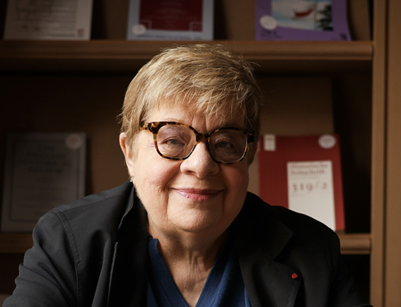 Portrait d’une femme souriante portant des lunettes devant une bibliothèque.