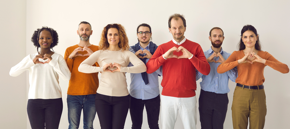Un groupe de six personnes de profils différents forme des cœurs avec leurs mains devant un fond clair.